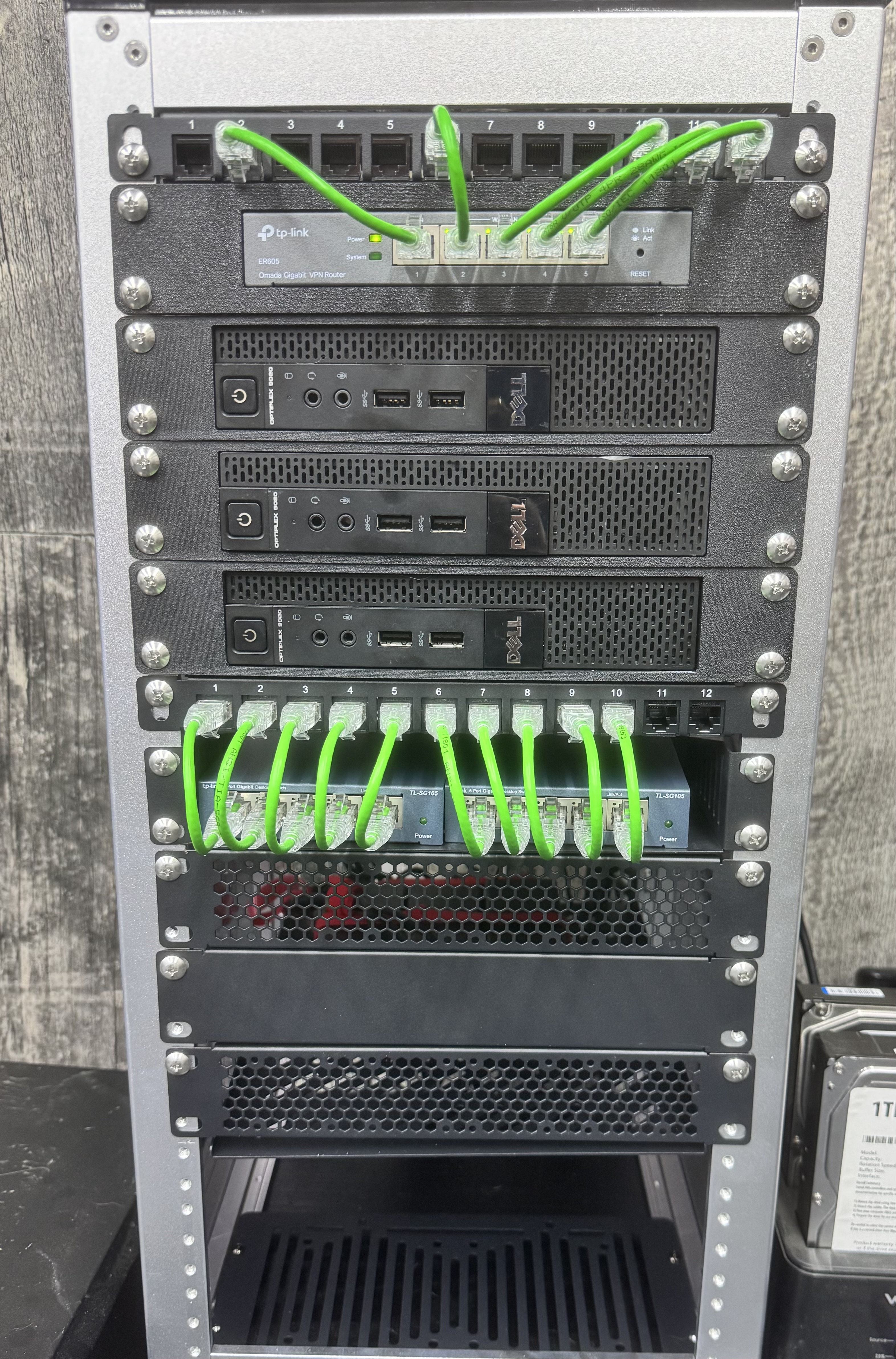 Rocknet Lab rack showing a patch panel, TP-Link ER605 router, three Dell OptiPlex compute nodes, and two TP-Link TL-SG105 switches wired with green patch cables